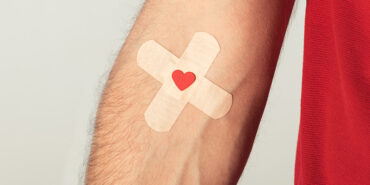 Partial view of patient in red t-shirt with plasters on grey background, blood donation concept