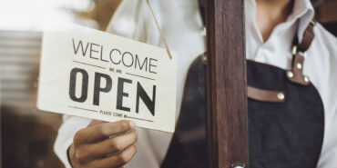 Store owner turning open sign broad through the door glass and ready to service.