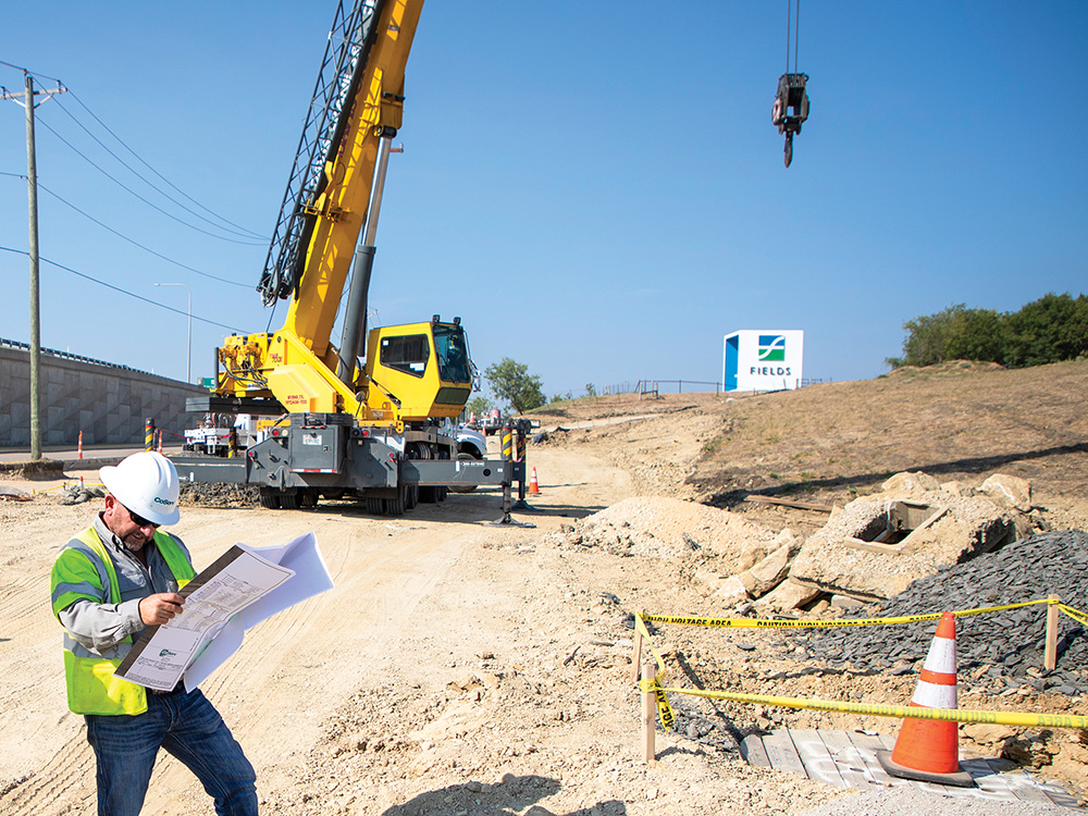 A crane prepares to lift the concrete pole while Slade checks the plans.
