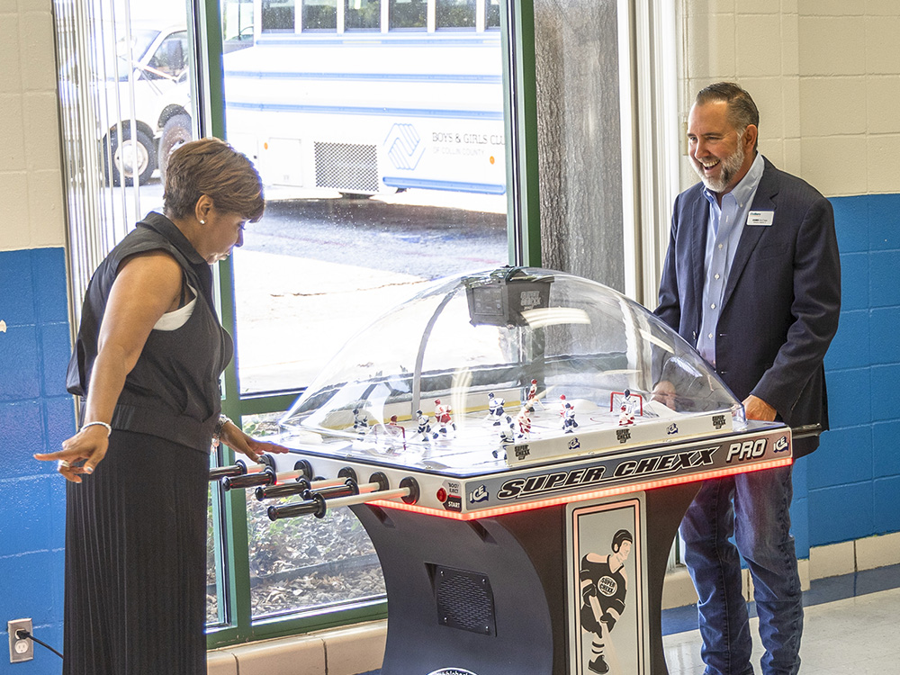 Boys & Girls Club of Collin County CEO Shawn Wills plays hockey with CoServ District 3 Board Director Chris McCraw. The commercial quality gaming station was purchased for the rec room thanks to a grant from the CoServ Charitable Foundation. 