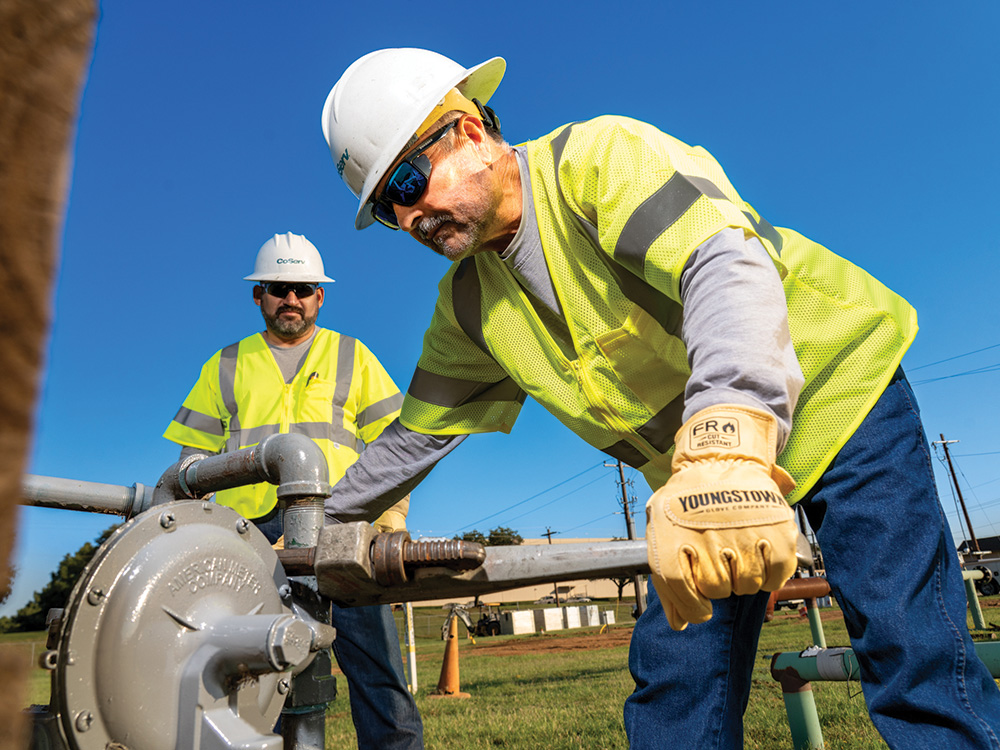Gas Service Operations Technician Tino Acosta checks pressure on a residential gas meter while Jose Abundiz assists.
