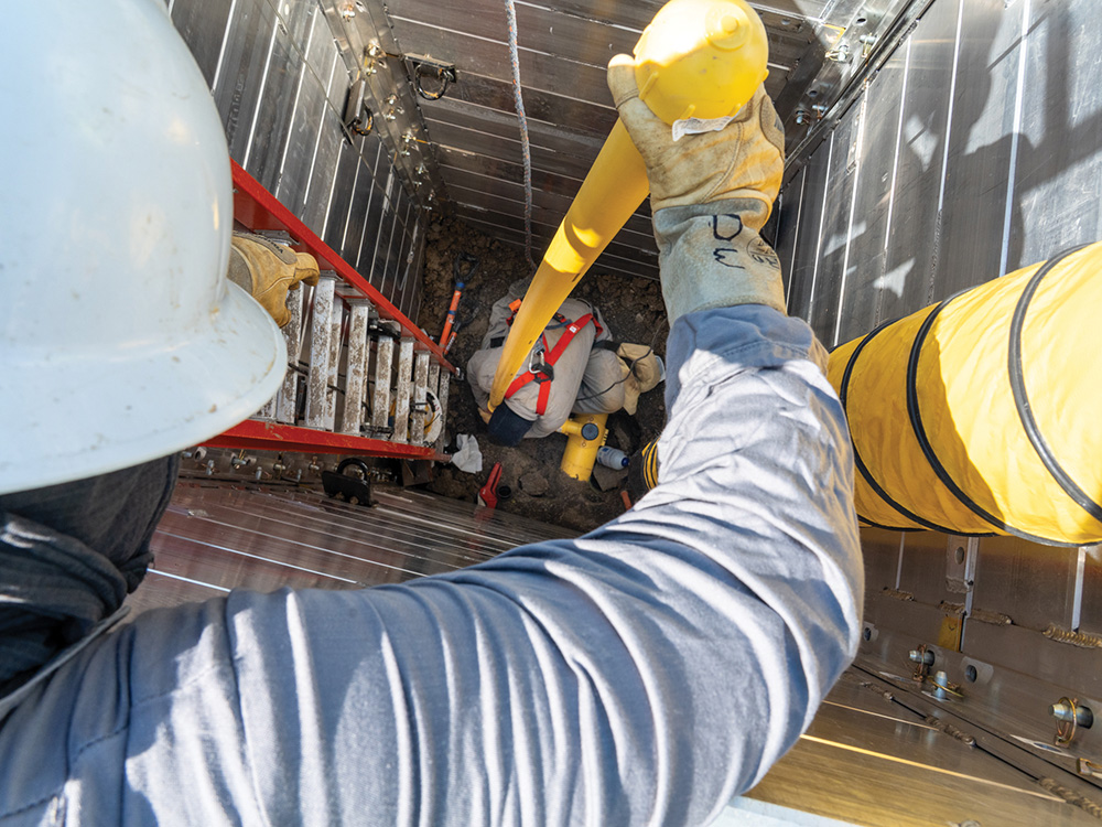 A gas construction crew connects a new service line inside shoring boxes.